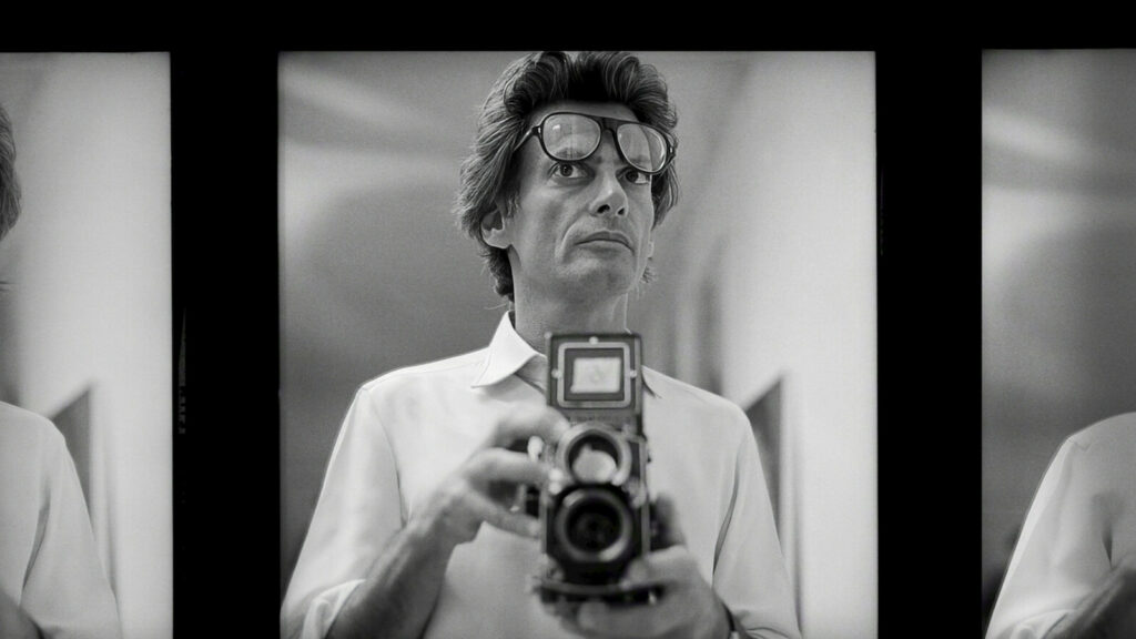Official Netflix artwork for Avedon: black and white contact-sheet frames of Richard Avedon holding a twin-lens camera at chest height, glasses pushed up on his head