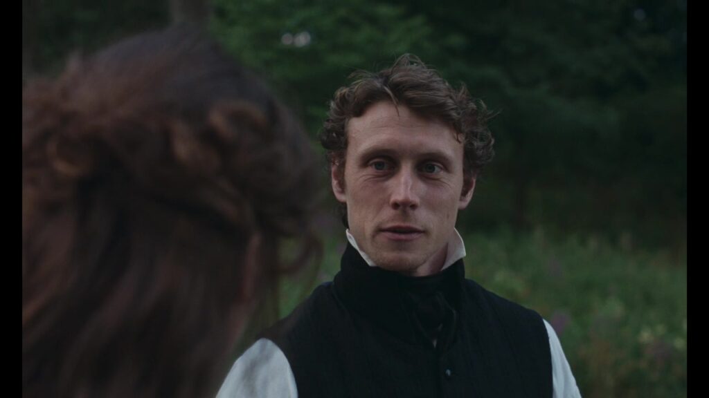 An intact frame from Sense and Sensibility Official Trailer 2 shows a young man in Regency dress speaking outdoors to a woman.