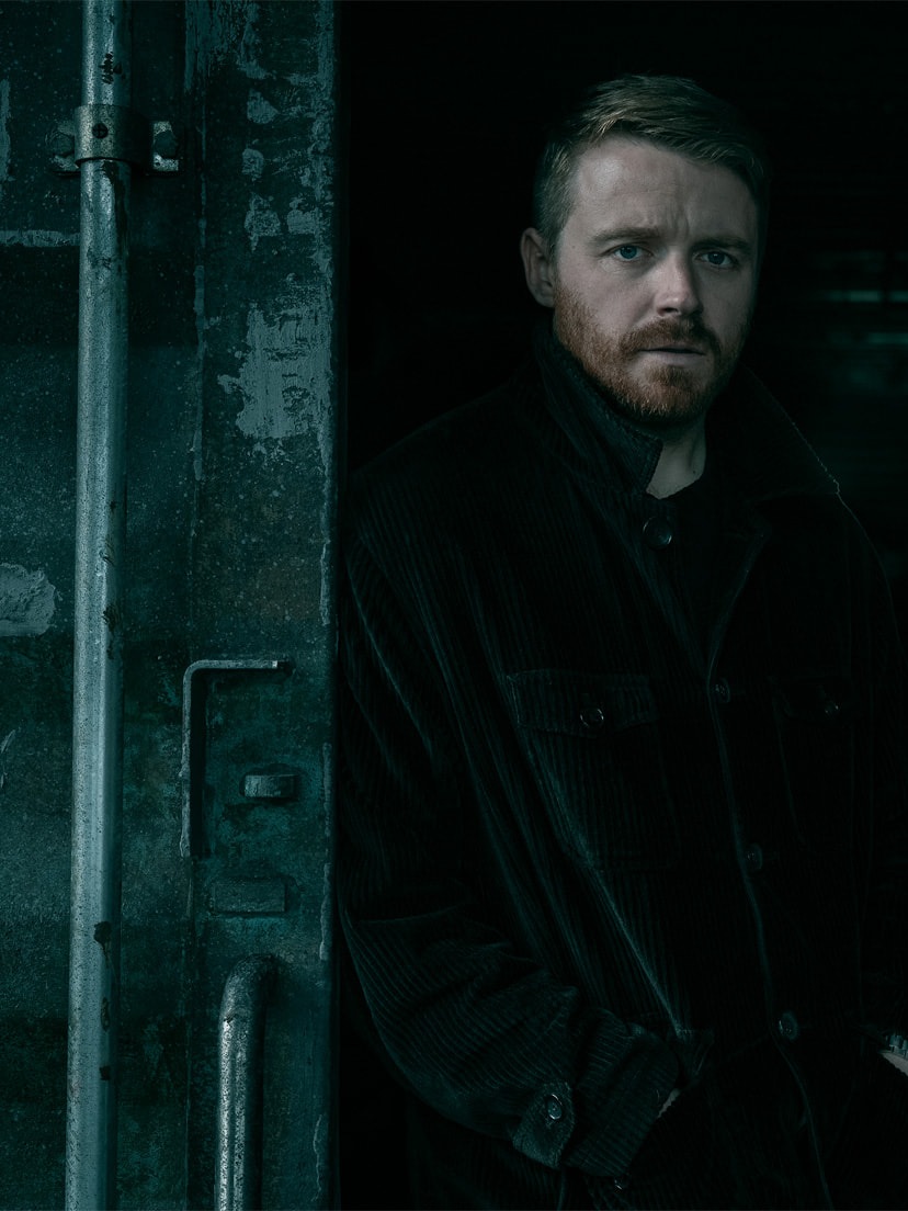 Jack Lowden in a dark jacket standing in a doorway in Slow Horses